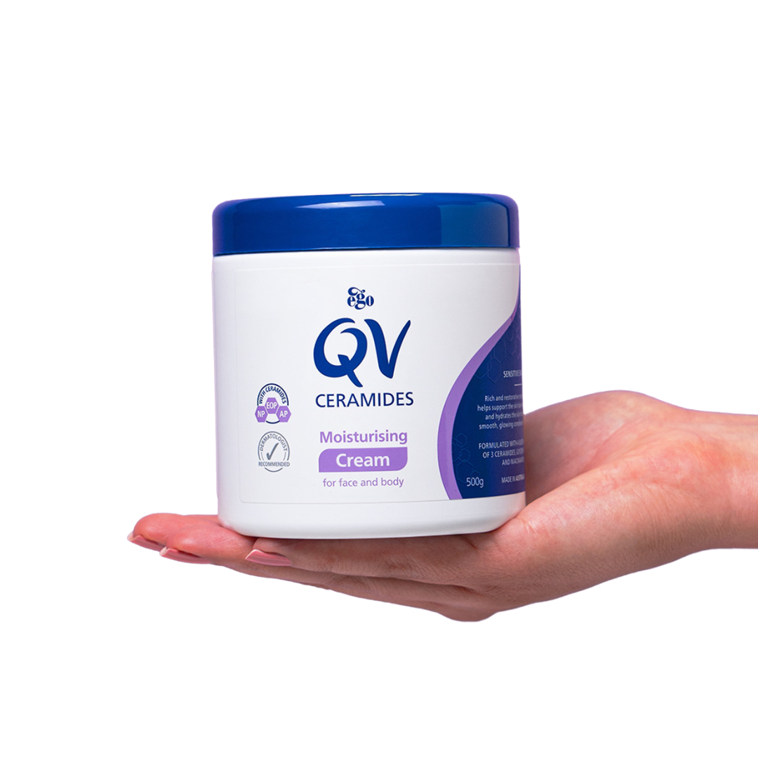 Hand holding a jar of QV Ceramides moisturizing cream against a white background